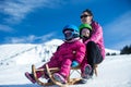 Mother and children having fun on sledge with panoramatic view of Alps mountains. Active mom and toddler kid with safety helmet. Royalty Free Stock Photo