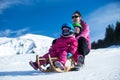Mother and children having fun on sledge with panoramatic view of Alps mountains. Active mom and toddler kid with safety helmet. Royalty Free Stock Photo