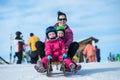 Mother and children having fun on sledge with panoramatic view of Alps mountains. Active mom and toddler kid with safety helmet. Royalty Free Stock Photo