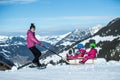 Mother and children having fun on sledge with panoramatic view of Alps mountains. Active mom and toddler kid with safety helmet. Royalty Free Stock Photo