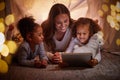 Mother and children live streaming on an app using a tablet in a tent camping at home at night. Happy mom and kids Royalty Free Stock Photo