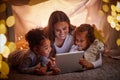 Mother and children live streaming movies on tablet or digital kids app in a tent camping at night and bokeh lights Royalty Free Stock Photo