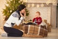 Mother comforts her little crying son on background of the Christmas tree.