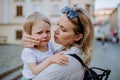 Mother consling her little daughter crying, holding her in arms in street in summer. Royalty Free Stock Photo