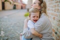 Mother consling her little daughter crying, holding her in arms in street in summer. Royalty Free Stock Photo