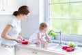 Mother and cury curly toddler washing vegetables