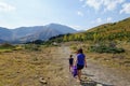 A mother and daugher hiking a beautiful trail above the treeline with a huge mountain in the background during a sunny fall day