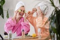 Mother and daughter in bathrobes and towels on head using natural cosmetics and having fun together at home Royalty Free Stock Photo