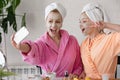 Mother and daughter in bathrobes and towels on head using natural cosmetics and having fun together at home Royalty Free Stock Photo