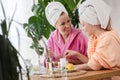 Mother and daughter in bathrobes and towels on head using natural cosmetics and having fun together at home Royalty Free Stock Photo