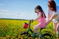 Mother and daughter with bicycle in a field with yellow dandelions. Family walks in the spring in nature Royalty Free Stock Photo