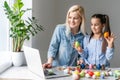 mother and daughter bloggers wearing rabbit ears headband sitting at kitchen at home. easter preparation coloring eggs