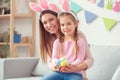 Mother and daughter in bunny ears together at home easter celebration sitting holding eggs looking camera