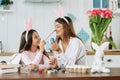 A mother and daughter celebrating Easter, painting eggs with brush. Happy family smiling and laughing, drawing on face. Royalty Free Stock Photo