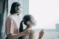 Mother with daughter child in mask looking from window Royalty Free Stock Photo