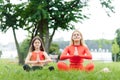 Mother and daughter doing yoga exercises on grass in the park at the day time. People having fun outdoors. Concept of friendly Royalty Free Stock Photo