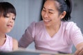 Mother and daughter drawing together with crayons. Adult woman helps girl study or draw together at home in living room. Happy