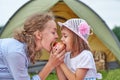 Mother and daughter eating apple near a tent in meadow or park. Happy family on picnic at camping Royalty Free Stock Photo