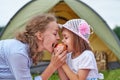Mother and daughter eating apple near a tent in meadow or park. Happy family on picnic at camping Royalty Free Stock Photo