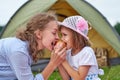 Mother and daughter eating apple near a tent in meadow or park. Happy family on picnic at camping Royalty Free Stock Photo