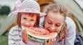 Mother and daughter eating watermelon near a tent in meadow or park. Happy family on picnic at camping Royalty Free Stock Photo