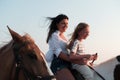 Mother and daughter enjoy riding horses together by the sea. Selective focus Royalty Free Stock Photo