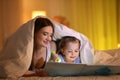 Mother and daughter with flashlight reading book under blanket Royalty Free Stock Photo