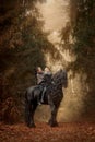 Mother and daughter with friesian horse walking in an autumn forest