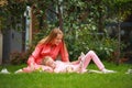 Mother with daughter in garden at home reading a book together on lawn grass under tree in garden of city park Royalty Free Stock Photo