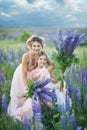 Mother and daughter gathering lupine flowers in beautiful field on sunset. Beautiful girl in violet dress holding a lupine at suns Royalty Free Stock Photo