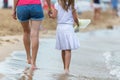 Mother and daughter girl walking together on sand beach in sea water in summer with bare feet in warm ocean waves Royalty Free Stock Photo