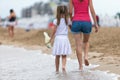 Mother and daughter girl walking together on sand beach in sea water in summer with bare feet in warm ocean waves Royalty Free Stock Photo