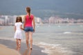 Mother and daughter girl walking together on sand beach in sea water in summer with bare feet in warm ocean waves Royalty Free Stock Photo