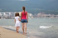 Mother and daughter girl walking together on sand beach in sea water in summer with bare feet in warm ocean waves Royalty Free Stock Photo