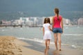 Mother and daughter girl walking together on sand beach in sea water in summer with bare feet in warm ocean waves Royalty Free Stock Photo