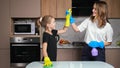 Mother and daughter with gloves clean white table in kitchen