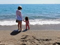 Mother and daughter hand in hand with bare feet in front of the beach with copy space