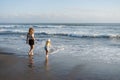 Mother with daughter have fun at beach with black sand in Bali, running at waves, enjoy life and traveling.