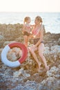 Mother daughter having fun resting on the rocky beach. Two blond lady wearing retro swimming suits enjoy summer day together Royalty Free Stock Photo