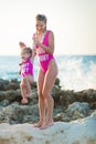 Mother daughter having fun resting on the rocky beach wearing pink swimming suits. Blond lady with girl enjoy summer time together Royalty Free Stock Photo