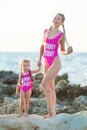 Mother daughter having fun resting on the rocky beach wearing pink swimming suits. Blond lady with girl enjoy summer time together Royalty Free Stock Photo