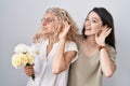 Mother and daughter holding bouquet of white flowers smiling with hand over ear listening an hearing to rumor or gossip Royalty Free Stock Photo