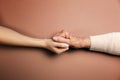 Mother and daughter holding hands. Close-up. Flat lay. Beige background. The concept of caring for pensioners