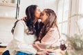 Mother and daughter hugging on kitchen window sill by decorated Christmas tree. Family spending time together at home Royalty Free Stock Photo