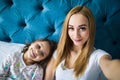 Mother and daughter lying on bed and taking self portrait with smartphone. Woman taking selfie on phone with a little girl in bedr