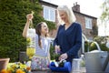 Mother And Daughter Making Recycled Plant Holders From Plastic Bottle Packaging Waste In Garden At Home