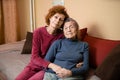 Mother and daughter, mature woman with red hair and elderly old cute happy lady woman with gray hair and deep wrinkles, embrace