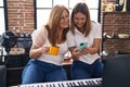 Mother and daughter musicians using smartphone drinking coffee at music studio