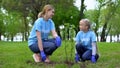 Mother and daughter planting bush in park together, environmental volunteering