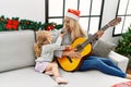 Mother and daughter playing guitar and singing sitting by christmas tree at home Royalty Free Stock Photo